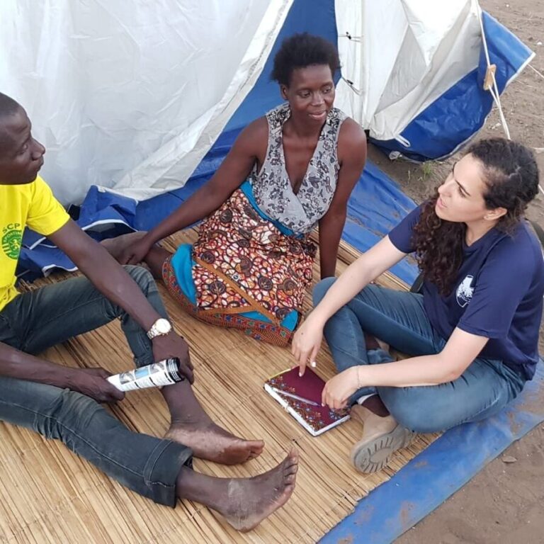 Two women sitting with a man and talking near a tent